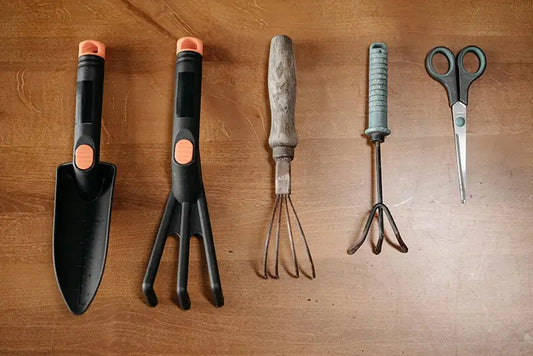 Flat lay of a 5-piece garden trowel set including trowel, transplanter, hand cultivator, weeder and hand rake with green handles on wooden surface