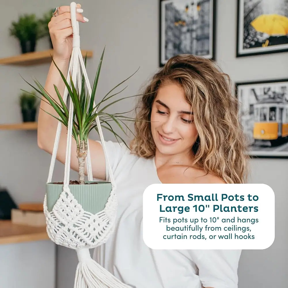 Woman holding a macrame plant hanger with a plant, in a home setting.