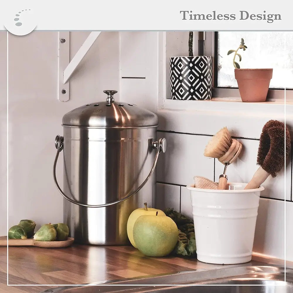 Stainless steel compost bin on a kitchen counter with apples and a white container.