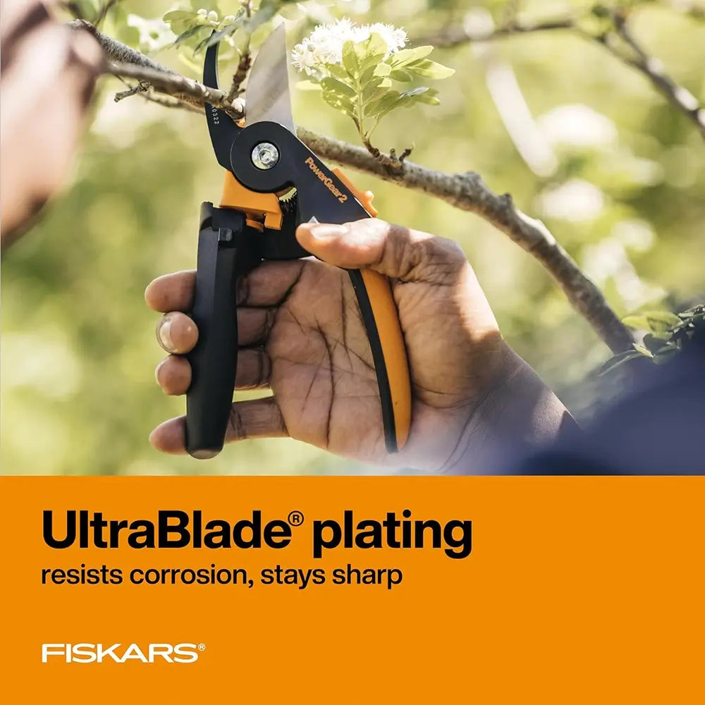 Hand holding Fiskars pruning shears with UltraBlade plating feature, against a blurred natural background.