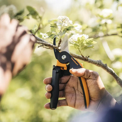 Hand holding a pair of garden shears with blurred greenery in the background