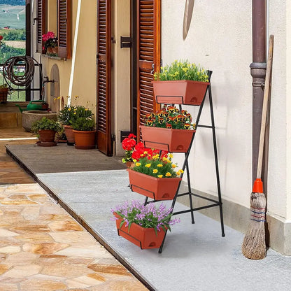 A black metal tiered plant stand holding four terracotta-colored rectangular planters filled with colorful flowers and greenery, set on a patio next to a house wall with shutters and a broom.