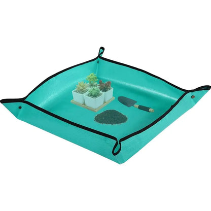 A square teal fabric garden bed liner with black trim and corner loops, shown empty on a white background. Small props inside include a small potted succulent, a trowel, and a pile of soil from our Indoor Garden Kit Essentials collection 