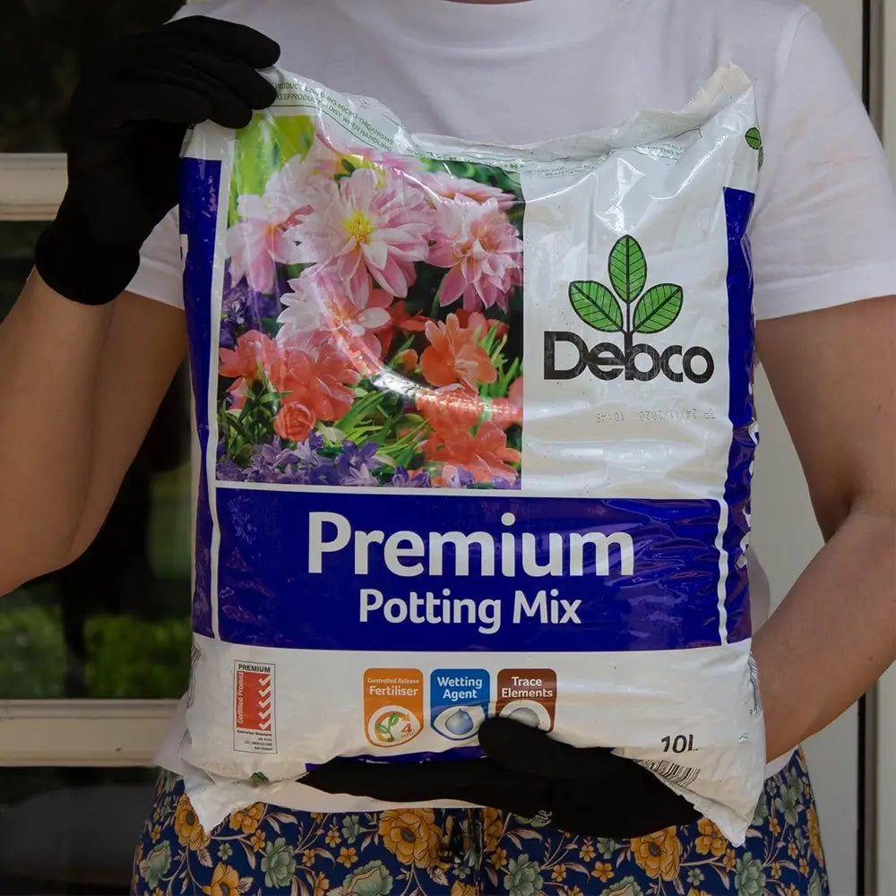 Person holding a bag of Debco Premium Potting Mix with floral design on packaging.