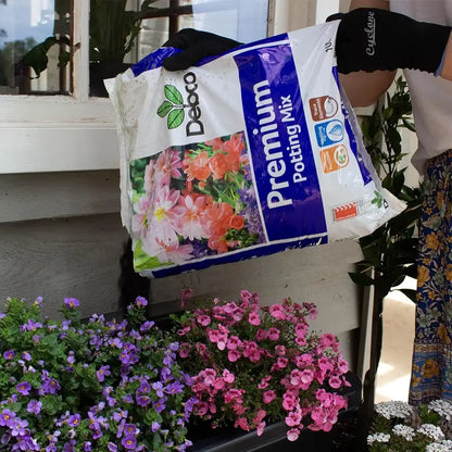 Person holding a bag of Debco Premium Potting Mix with flowers in the foreground