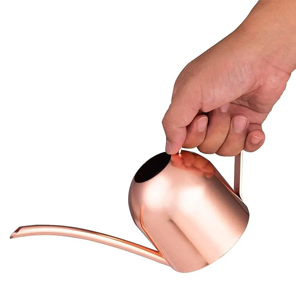 Copper watering can held by a hand on a white background