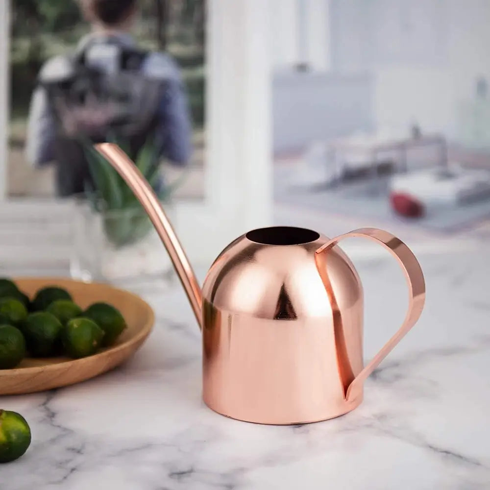 Rose gold watering can on a marble surface with limes and a blurred background