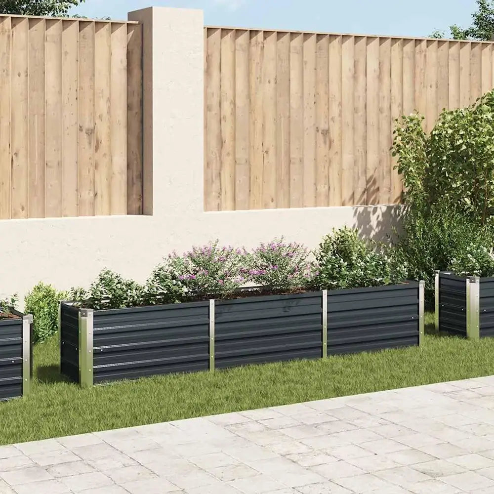 Row of black metal planters with greenery against a wooden fence.